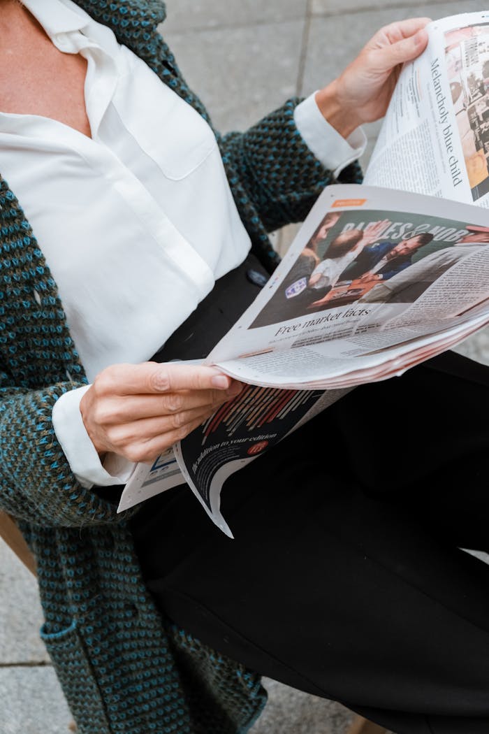 A woman reading a newspaper in an outdoor setting, capturing a moment of relaxation and information gathering.